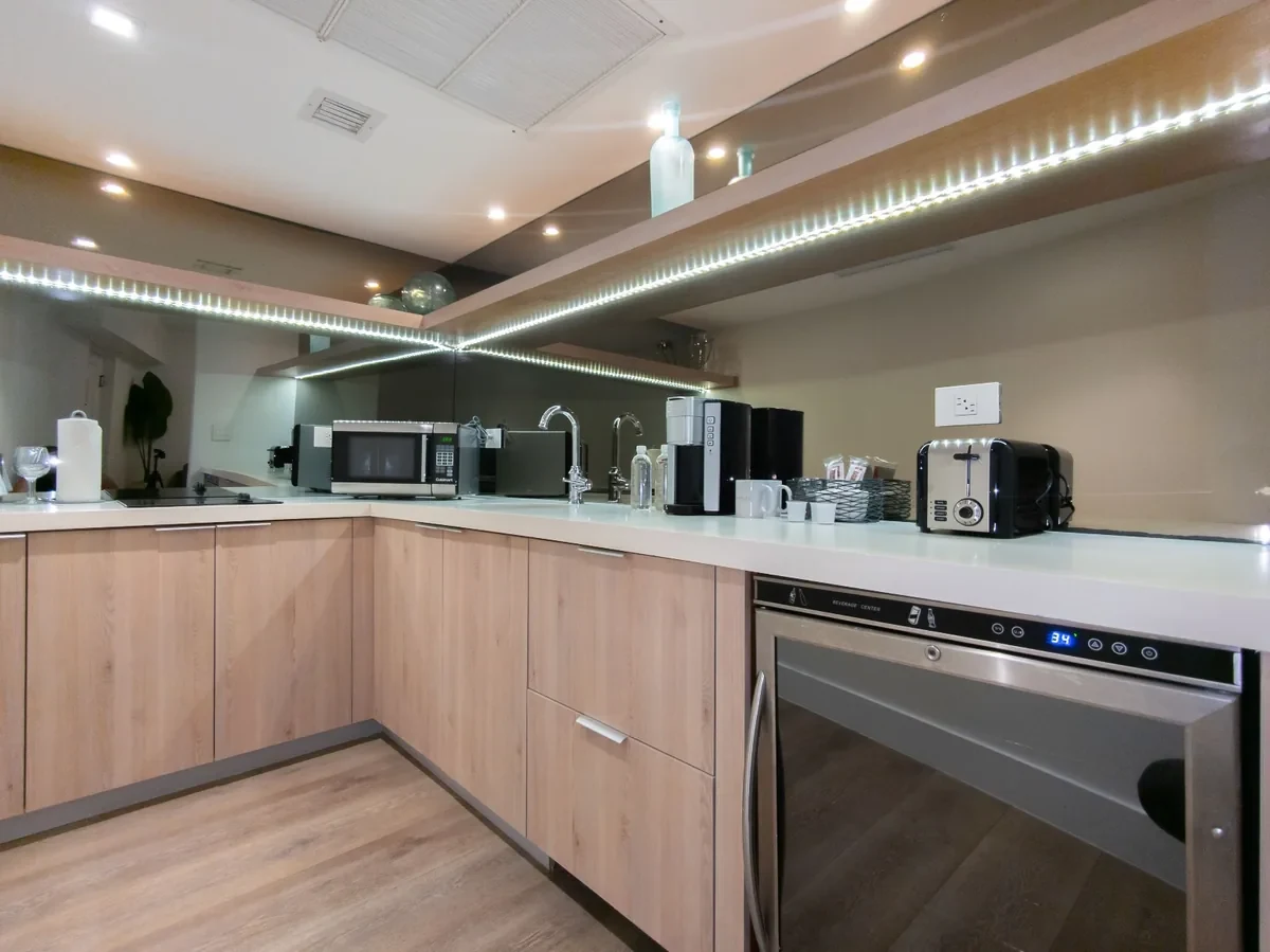Boutique hotel kitchenette at Bentley Hotel South Beach — light oak cabinetry, LED strip cove lighting, mirrored backsplash, wine cooler, Nespresso and toaster, IV Atelier hospitality interior design Miami Beach