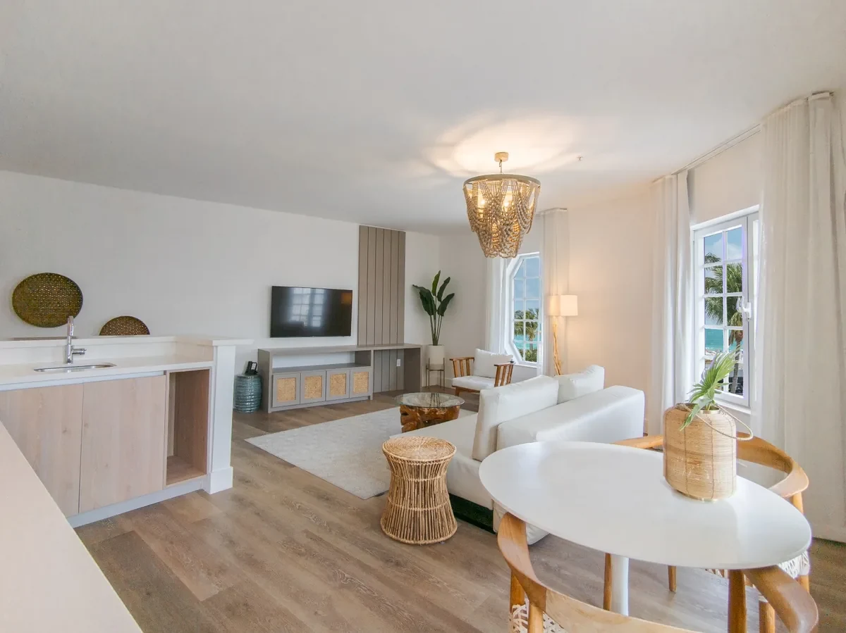 Boutique hotel suite at Bentley Hotel South Beach — beaded chandelier, white sofa, rattan stool, ocean view through large windows with linen curtains, IV Atelier South Beach hotel renovation