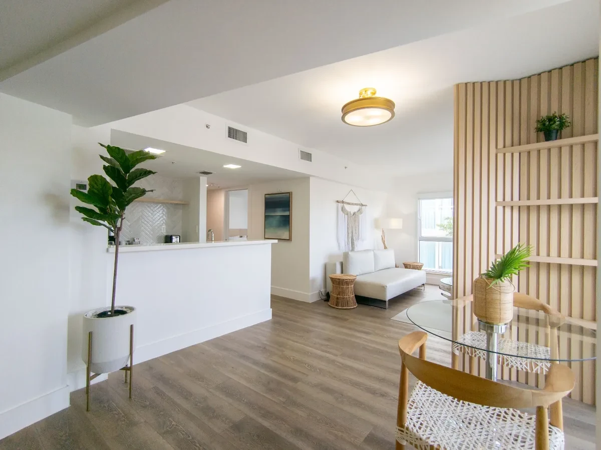 Open-plan boutique hotel suite at Bentley Hotel South Beach — view from entry through slatted wood divider to dining area and living room with herringbone kitchenette, IV Atelier Ocean Drive renovation