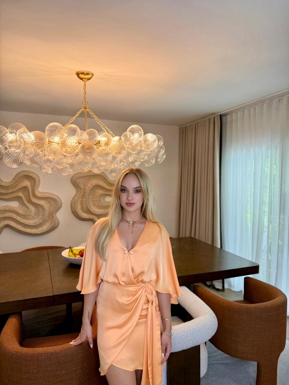 Irena Viitiuk, founder and principal designer of IV Atelier, photographed in a completed dining room interior — custom dark walnut table, sculpted terracotta chairs, oversized glass bubble chandelier and organic plaster wall art, Miami luxury interior design