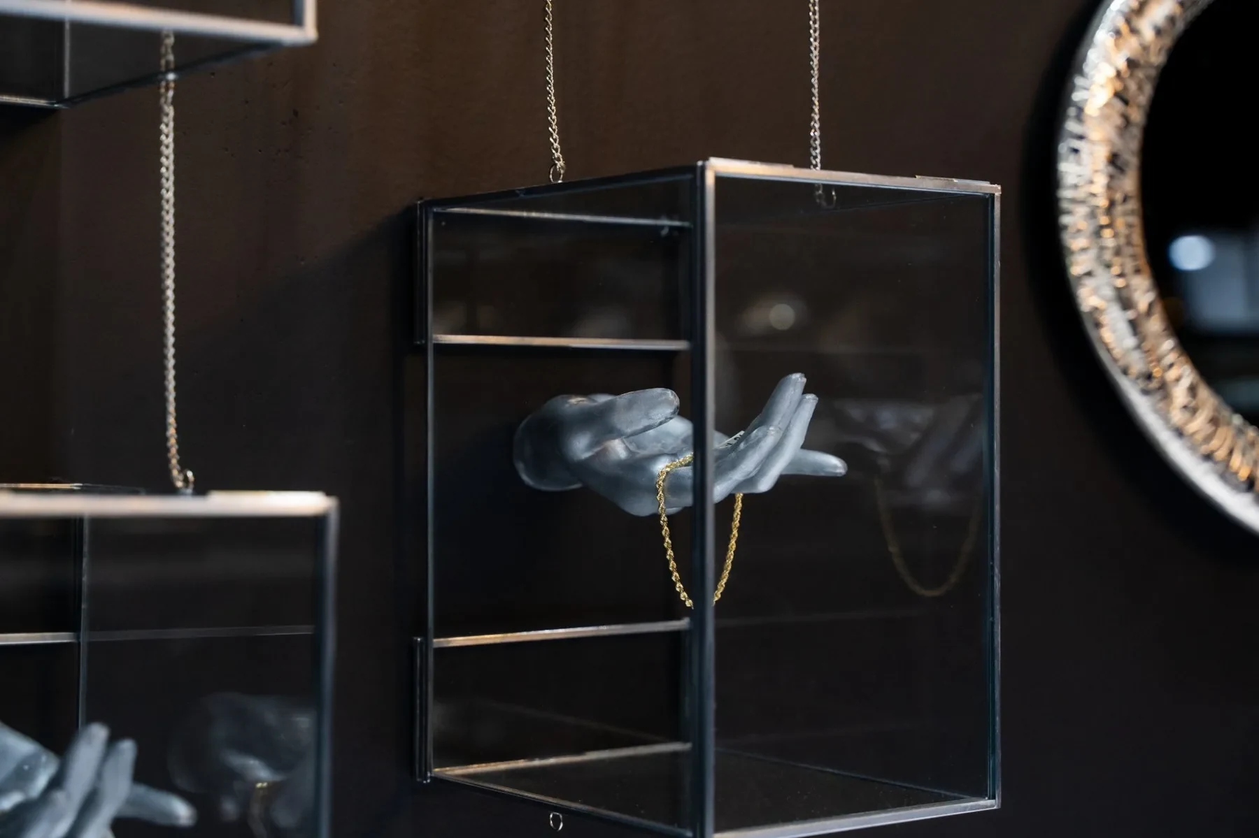 Luxzen suspended glass display box with hand sculpture and gold chain.