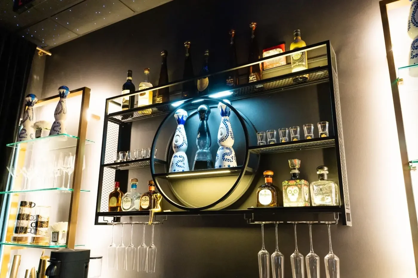 Luxzen bar — circular shelf with Don Julio bottles and hanging glassware.