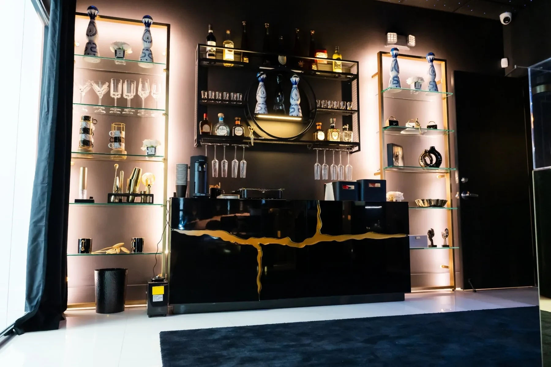 Luxzen bar wall — black lacquer counter with illuminated spirit display shelves.