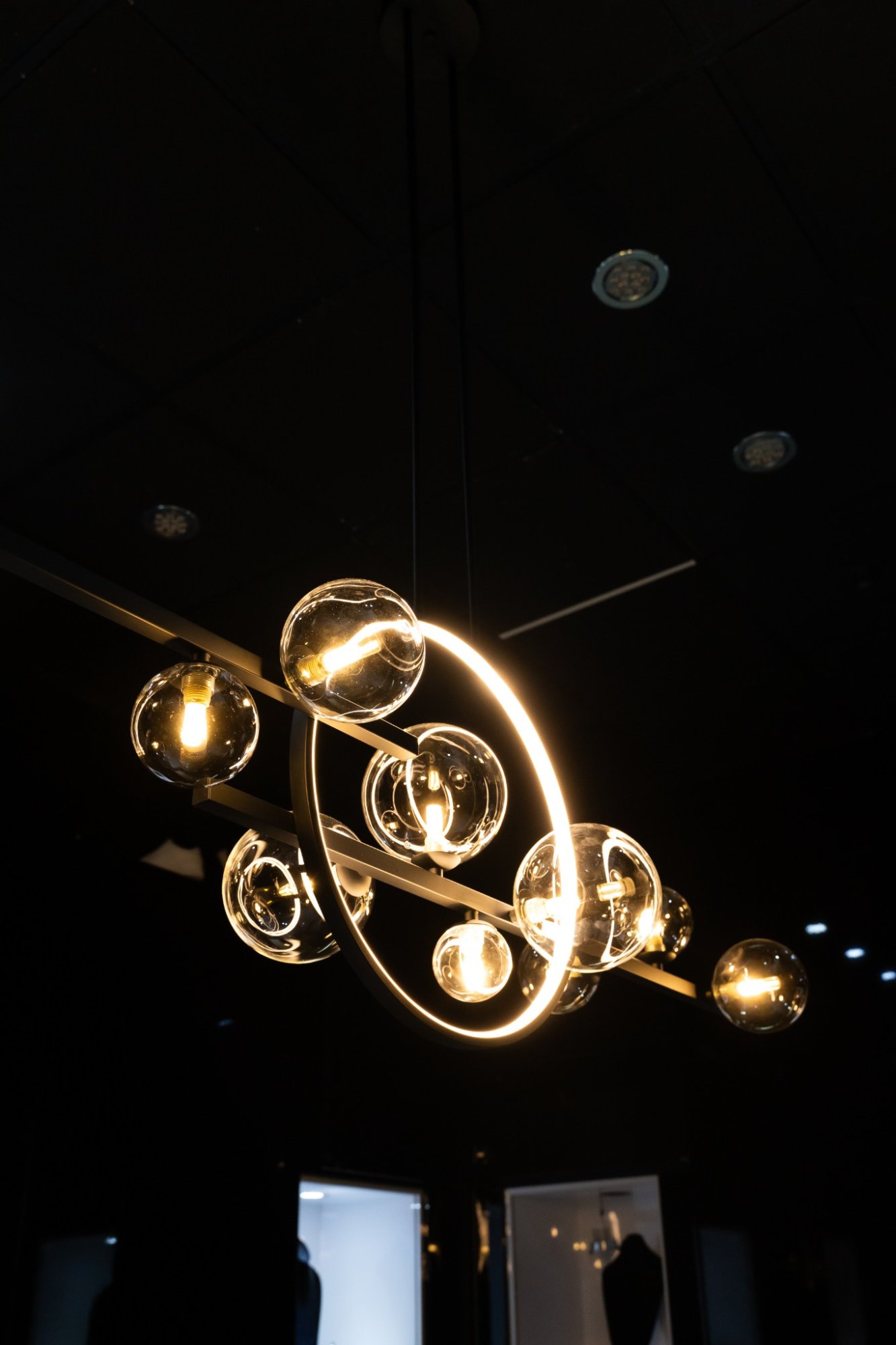Luxzen chandelier — brass ring and globe sculpture against dark ceiling.