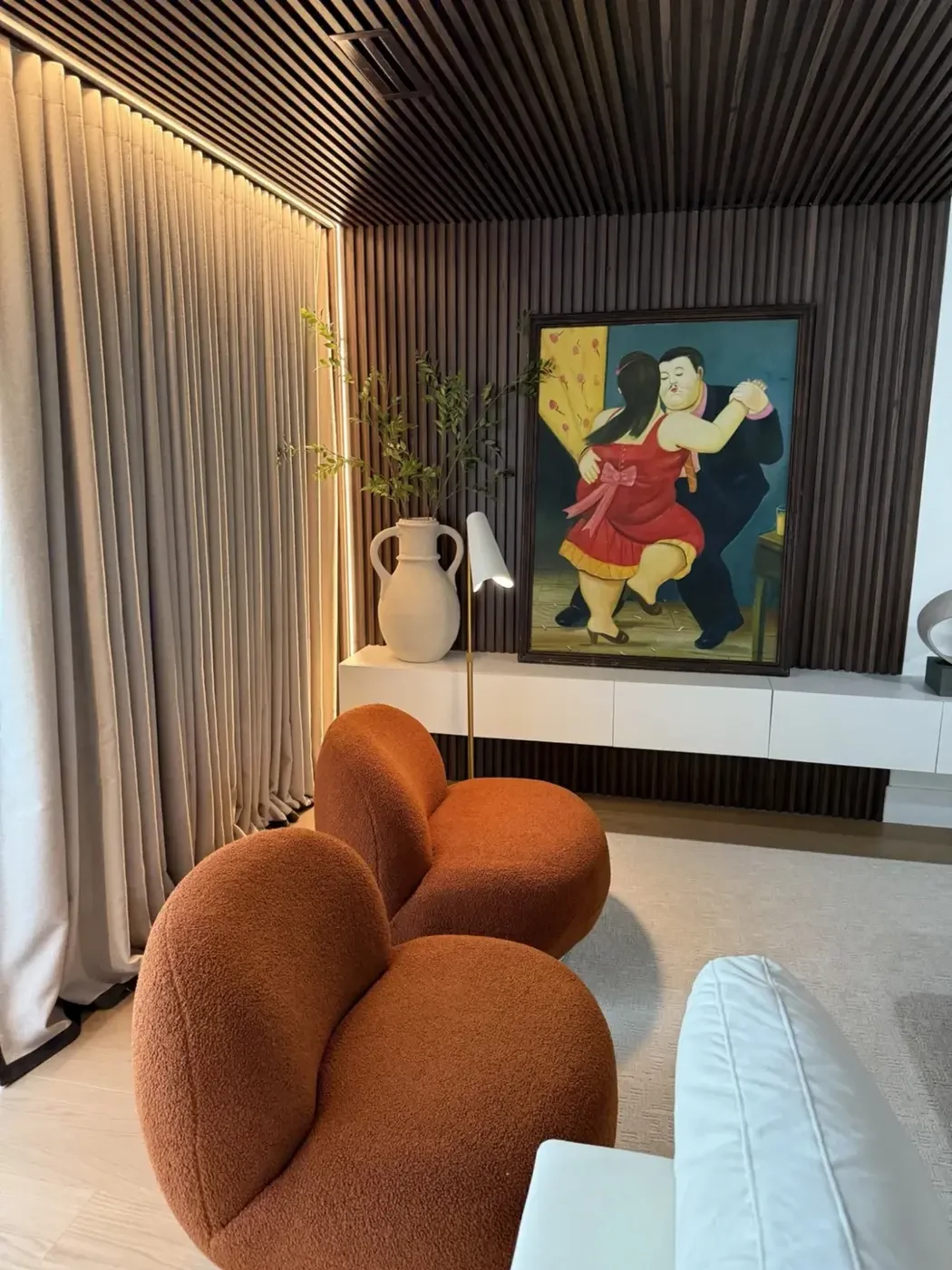 San Souci Residence — media wall with slatted wood, Botero painting and orange boucle lounge chair.