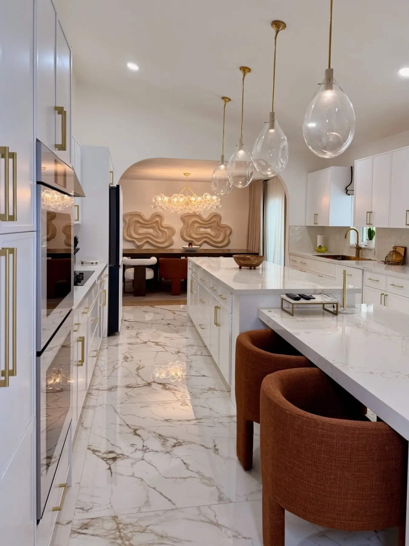 San Souci Residence — kitchen with white cabinetry, gold hardware and glass pendants looking into dining room.