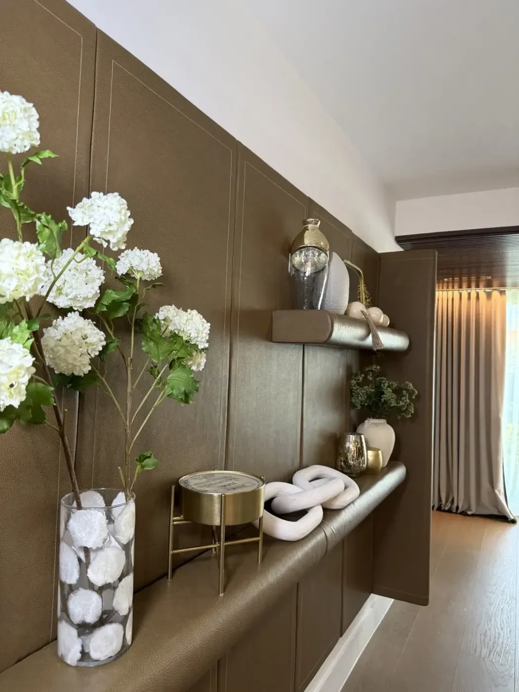 San Souci Residence — leather feature wall with floating shelves and white hydrangea arrangement.